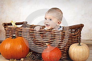 Little baby boy sitting in the basket with pumpkins