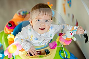 Little baby boy sitting in a colourful baby Walker with toys and