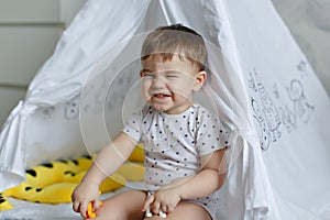 Little baby boy sitting in a tepee tent and funny wrinkles his n
