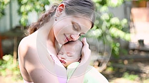 Little baby boy sleeping on mom`s chest outdoor. mother hugging sleeping baby in her arms and kissing the kid gently