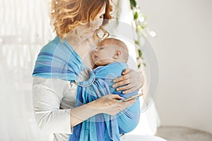 Little baby boy sleeping tight with open mouth and sweet face expression in baby sling while mom resting reading world