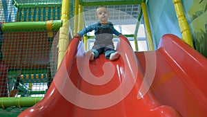 A little baby boy sliding on slide in a ball pool.