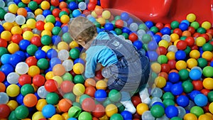A little baby boy sliding on slide in a ball pool.