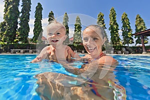 Little baby boy swimming in outdoor pool with mother