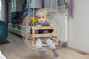 Little baby boy is swinging in swing at home