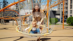 Little baby boy swinging in swing with mother. Children playing outdoor, kids outside, summer holiday and vacation