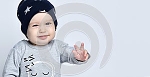 Little baby boy toddler in grey casual jumpsuit, black cap with starssmiling and gesticulating