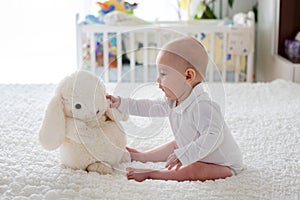 Little baby boy, toddler, playing at home with plush toy in bed