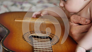 Little baby boy touches and tugs strings of vintage acoustic guitar. Infants and toddlers concept. Front view close up