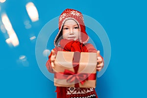 Little baby boy wear santa suit smile and show gift box with red bow on blue background. selected focus. christmas time