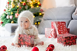 Little baby boy in white knitted onesie, playing with and opening presents at home