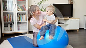 Little baby boy with young mother doing fitness on fitball in living room. Concept of healthcare, sports, yoga and kids
