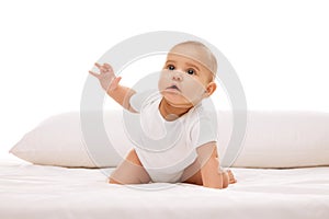 Little baby child, girl, infant in white onesie crawling on bed with pillow, looking upwards with attention and