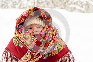 A little baby  in  a colorful  headscarf against the backdrop of a winter snowy forest