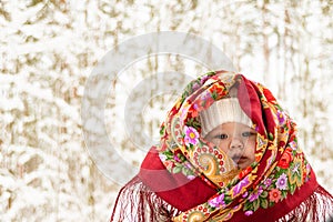 A little baby  in  a colorful  headscarf against the backdrop of a winter snowy forest