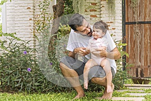 Little baby daughter sitting on her father scoop while rest in the garden at home. Handsome single dad holding and