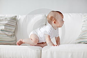 Little baby in diaper crawling along sofa at home
