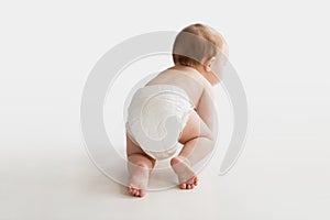 Little baby in diaper crawling on white floor