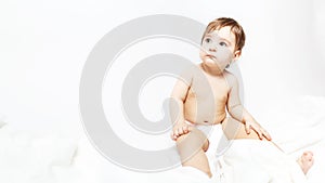 little baby in a diaper. Portrait of a cute baby 9 months old sitting on a white blanket