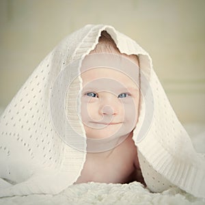 Little baby with Down syndrome hid under blanket and smiles slyly