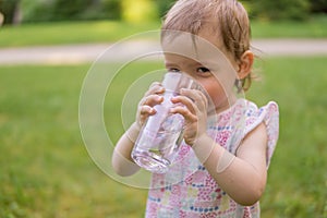 Little baby is drinking water from glass at sunny hot day