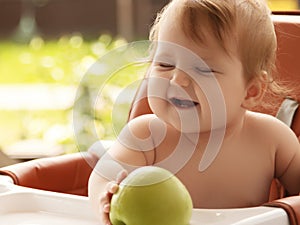 Little baby eating fruit puree outdoors. little smiling girl sits in baby-chair and have a breakfast. baby
