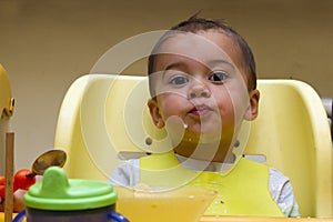 Little baby eats with a spoon soup plate. He sits on a children`s chair, putting foods