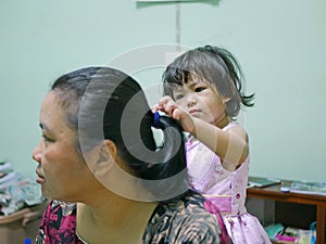 Little baby girl, 2 years old, enjoys playing / pretending to do her auntie`s hairs at home