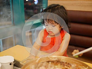 Little baby girl is addicted to a smartphone, keeps watching video streaming, while ignoring the meal in front of her