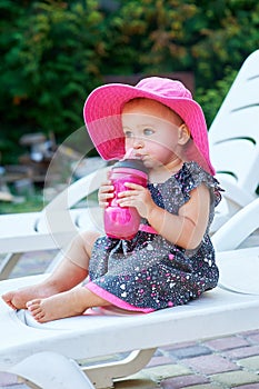 Little baby girl in autumn park drinks from pink plastic bottle