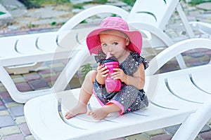 Little baby girl in autumn park drinks from pink plastic bottle