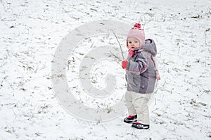 Little baby girl beautiful winter day playing in the snow wearing a jacket hooded down jacket, trousers, hat and gloves