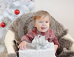 Little baby girl with big gift in hands near Christmas tree