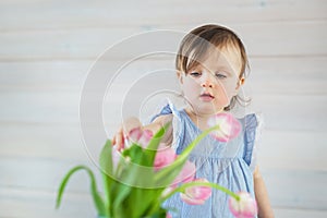 Little baby girl in a blue dress touches a tulips