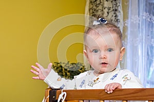 Little baby girl with bow on her head plays in the crib