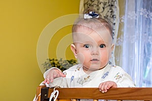 Little baby girl with bow on her head plays in the crib