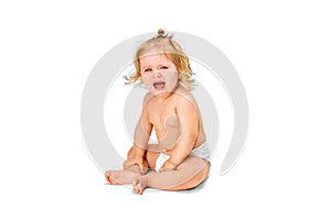 Little baby girl, child, toddler in diaper sitting on floor and crying against white studio background. Upset