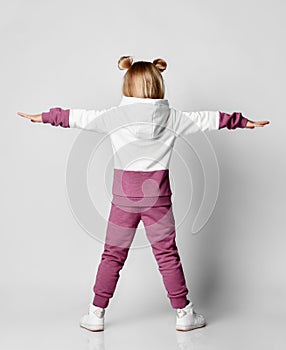 Little baby girl in a colorful sports suit stands with his back to the camera.