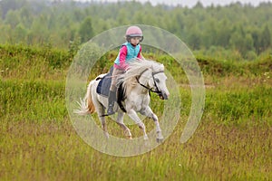 Little baby girl confident riding a horse at a gallop across the field