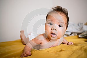 Little baby girl crawling in bed at home with happy face on yellow sheet close up. Crawling is the first childhood milestone