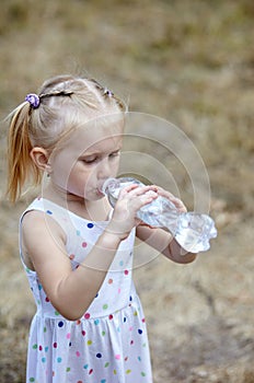 Little baby girl drinks water from a bottle in the park