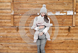 Little baby girl and her mother babywearing the ergo carrier in winter wooden background