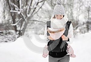 Little baby girl and her mother walking outside in winter Mother is holding her baby babywearing in the ergo carrier