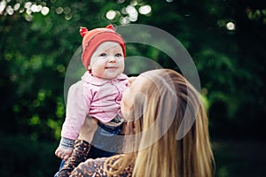 Little baby girl and her mother walking in the park. Red hat. Blue eyes.