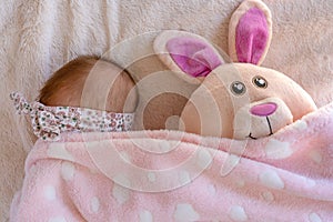 little baby girl hiding under her blanket with her easter bunny plush cuddly soft toy