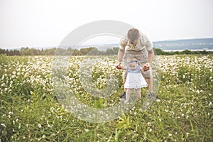 Little baby girl and his father enjoying outdoors in field of daisy flowers