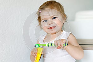 Little baby girl holding toothbrush and brushing first teeth. Toddler learning to clean milk tooth.