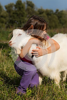Little Baby Girl Hugs A Goat In Village In Summer Close Up