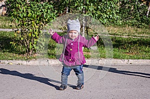 Little baby girl in jeans jacket and hat making learning to walk his first steps on the lawn in the green grass