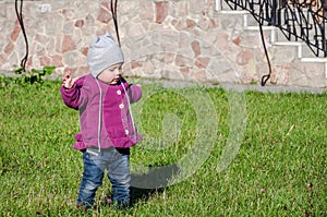 Little baby girl in jeans jacket and hat making learning to walk his first steps on the lawn in the green grass